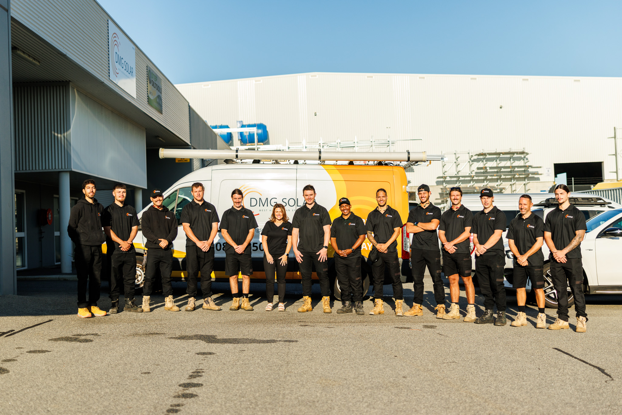 Meet the Team: A group of 13 people wearing matching black uniforms stands in a row outside a commercial building, with two service vans parked behind them in the sunlight. Meet the Team: A group of 13 people wearing matching black uniforms stands in a row outside a commercial building, with two service vans parked behind them in the sunlight.