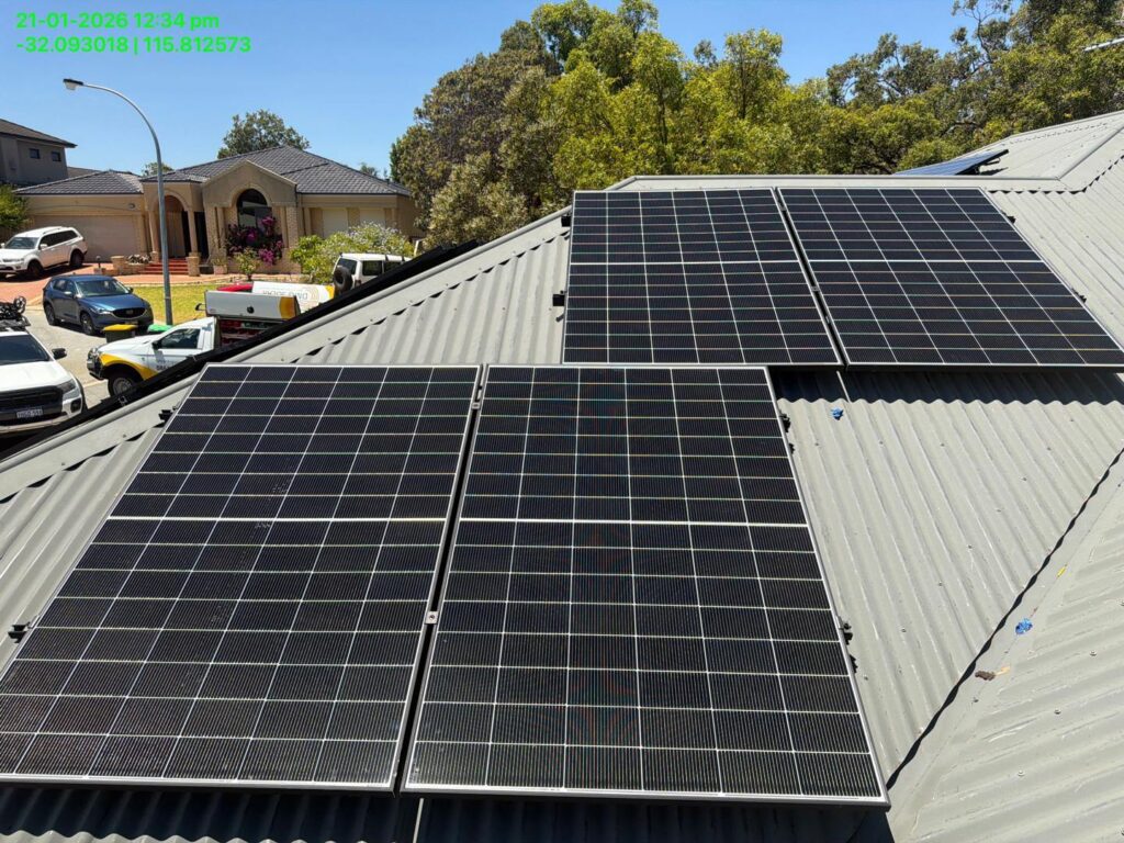 Four 9.975kW solar panel arrays installed on a corrugated metal roof in Bibra Lake. Trees, houses, and vehicles are visible nearby. Text with date, time, and coordinates appears in the top left corner. 50.5kWh battery storage included.