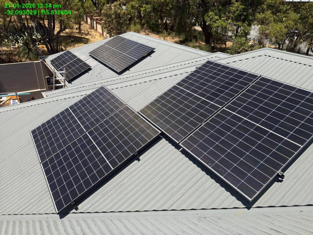 Solar panels are installed on the grey metal roof of a building in Bibra Lake, surrounded by trees. Multiple 9.975kW solar panels capture sunlight for energy generation, supported by 50.5kWh battery storage. The photo includes a timestamp and GPS coordinates.