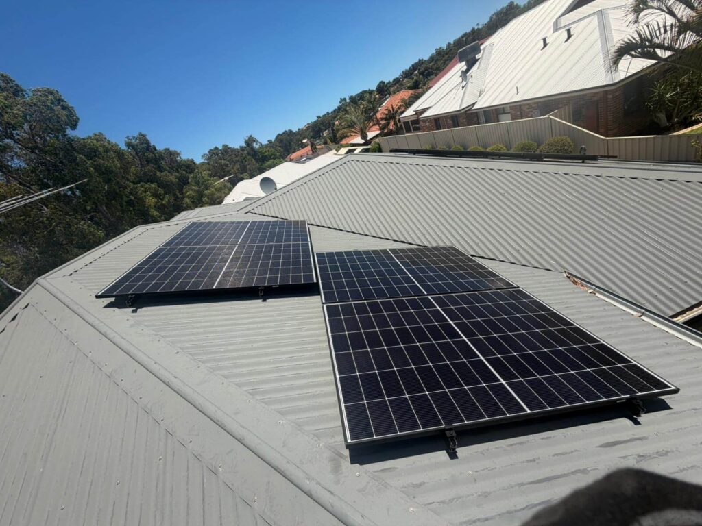 Two sets of 9.975kW solar panels are installed on the metal roof of a Bibra Lake home under a clear blue sky, with trees and neighbouring rooftops in the background, complemented by 50.5kWh battery storage.