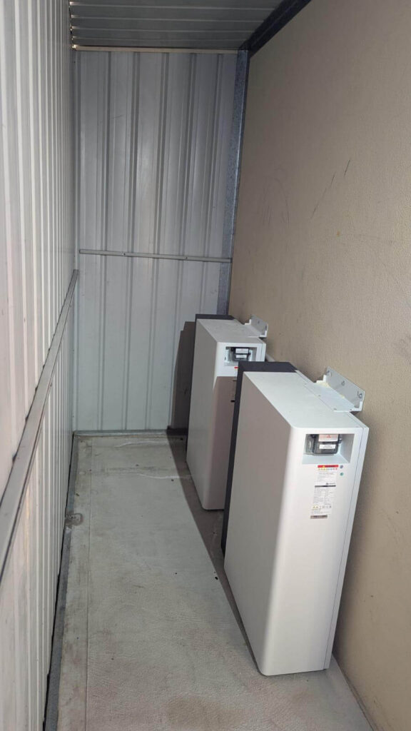 Two white air conditioning units are installed side by side in a narrow, enclosed metal space with bare walls and a concrete floor—typical of utility rooms in Canning Vale, often used for solar installation or battery storage set-ups.