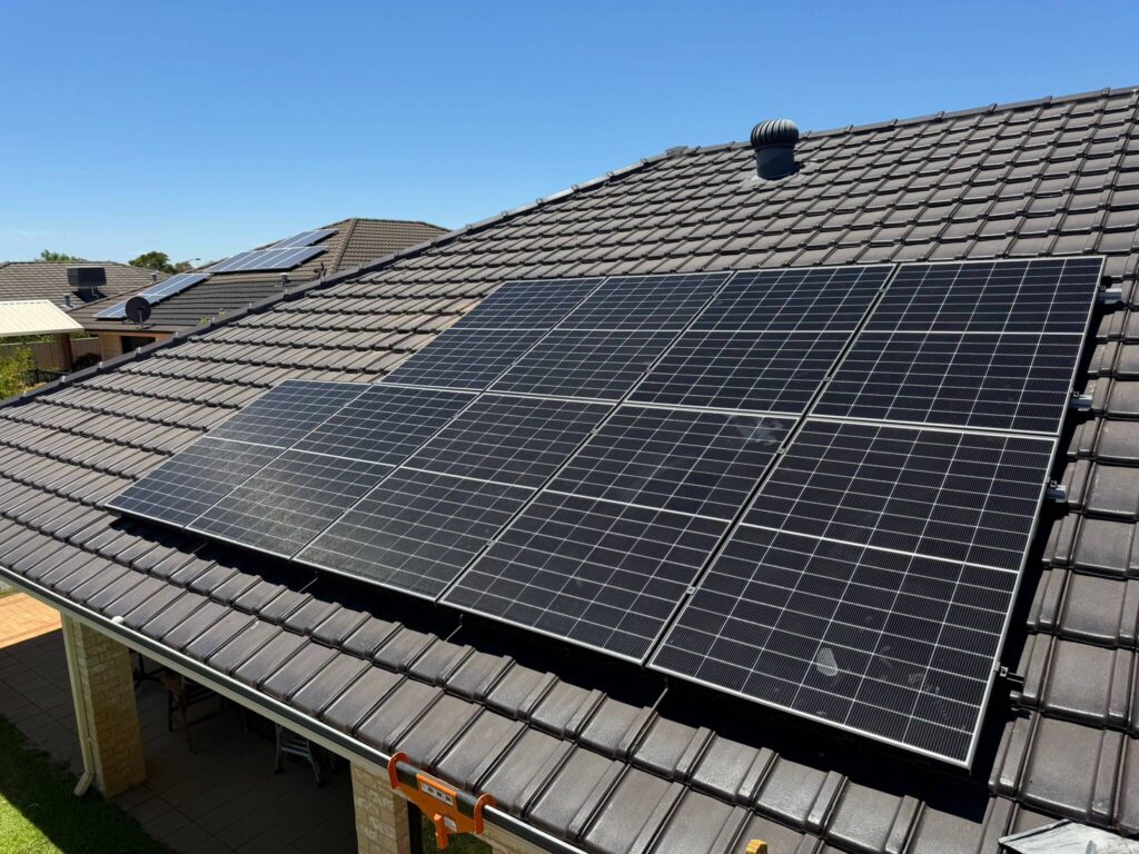 Solar panels installed on the sloping roof of a house in Canning Vale under a clear blue sky, with similar panels visible on a neighbouring rooftop. Battery storage solutions may also complement these solar systems for added efficiency.
