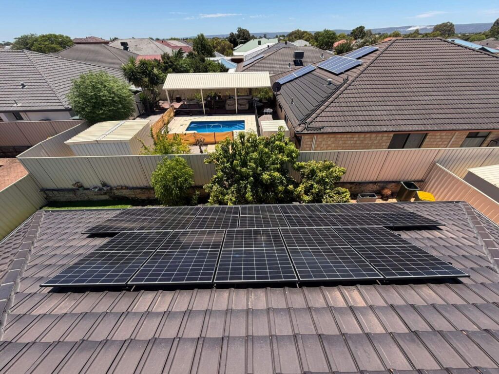 Rooftop view of a 9.975kW solar system installed on a Canning Vale house, with neighbouring rooftops, a back garden pool, trees, and clear sky in the background.