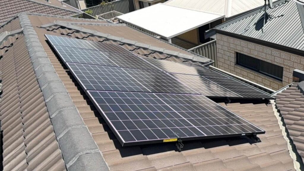 Solar panels installed on the tiled roof of a residential house, paired with 7.125 kW solar and a 5kW inverter, capture sunlight for energy generation. Nearby rooftops and a satellite dish are visible in the background.