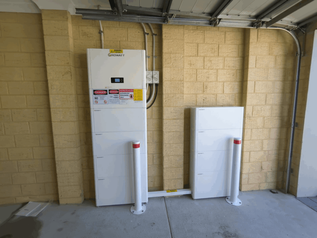 A Growatt DC-Coupled Storage System and inverter unit, providing 40 kWh capacity, are installed against a beige brick wall in a Landsdale garage, with safety bollards and warning labels visible on the equipment.