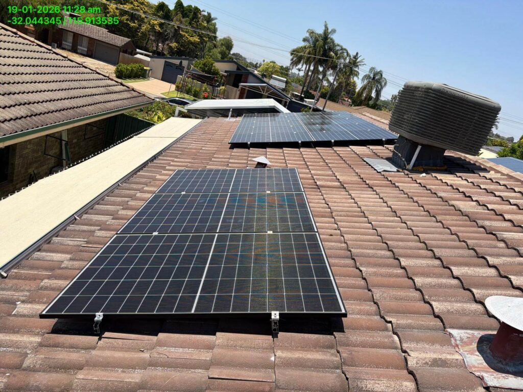 Several 9.975kW solar panels are installed on the tiled roof of a Parkwood house under a clear blue sky, with trees and other homes in the background. A large water tank and 50.5kWh battery storage system sit nearby on the roof.
