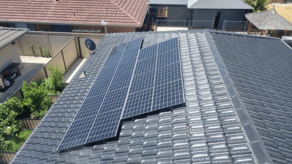 Solar panels with 9.97 kW solar capacity are installed on the dark grey tiled roof of a house in Southern River, surrounded by other homes and green plants; battery storage enhances energy efficiency for this residential neighbourhood.