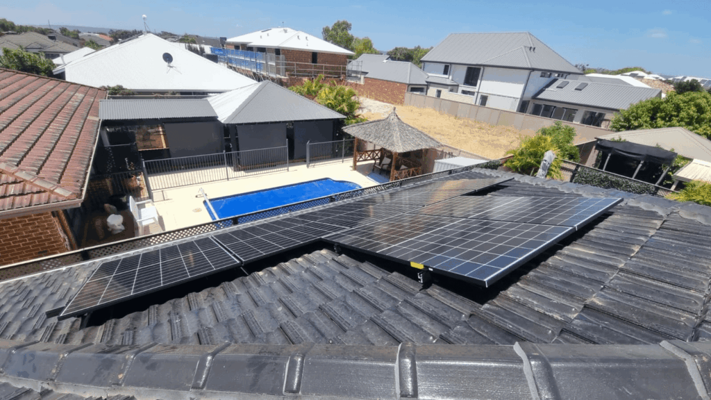 9.97 kW solar panels installed on a tiled rooftop in Southern River overlook a back garden with battery storage, a fenced swimming pool, patio area, and surrounding houses under a clear blue sky.
