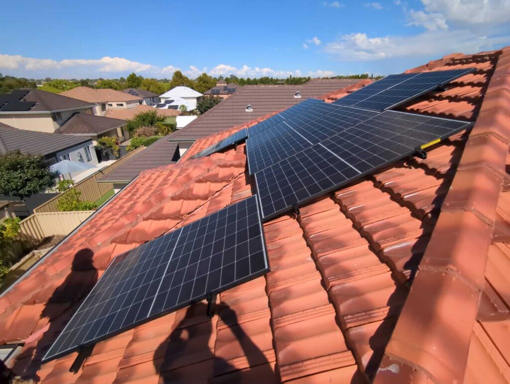 Solar panels installed on the sloped, red-tiled roof of a house in suburban Stirling, featuring an 11 kW solar system paired with Growatt battery storage, surrounded by greenery and neighbouring homes on a sunny day.