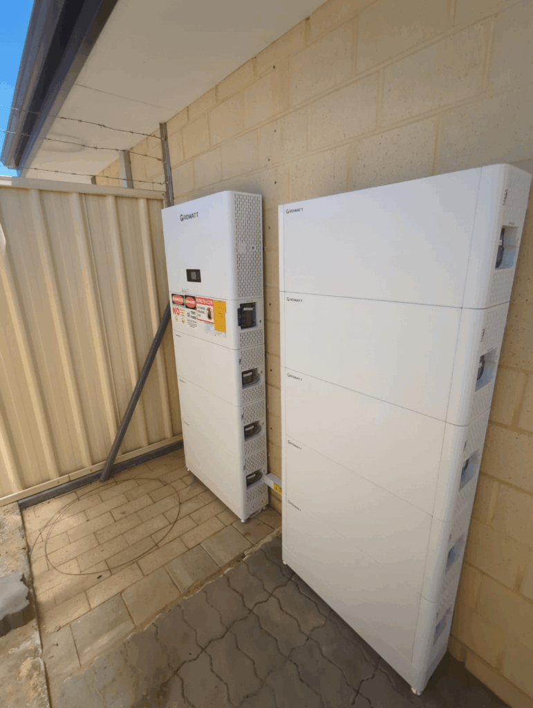 Two white Growatt AC-coupled storage system units, offering 40 kWh capacity, are installed against a beige brick wall outside in Swan View, next to a metal fence. The ground is paved with bricks and sunlight casts shadows on the setup.