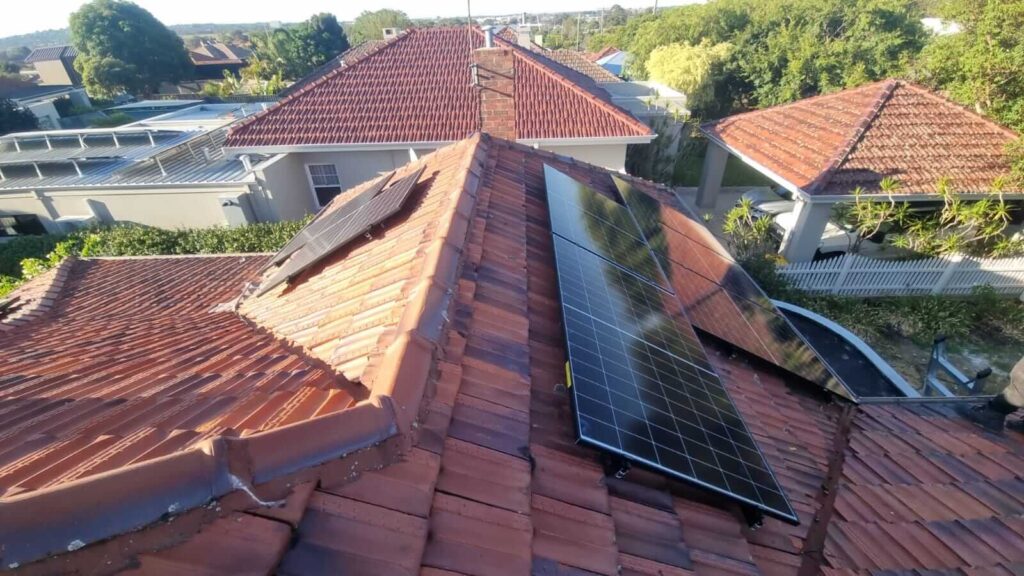 Red-tiled house roof in Wembley with a 9.5kW solar system and 40kWh battery storage installed across different sections, surrounded by trees and nearby homes with similar roofs, seen from an elevated angle.