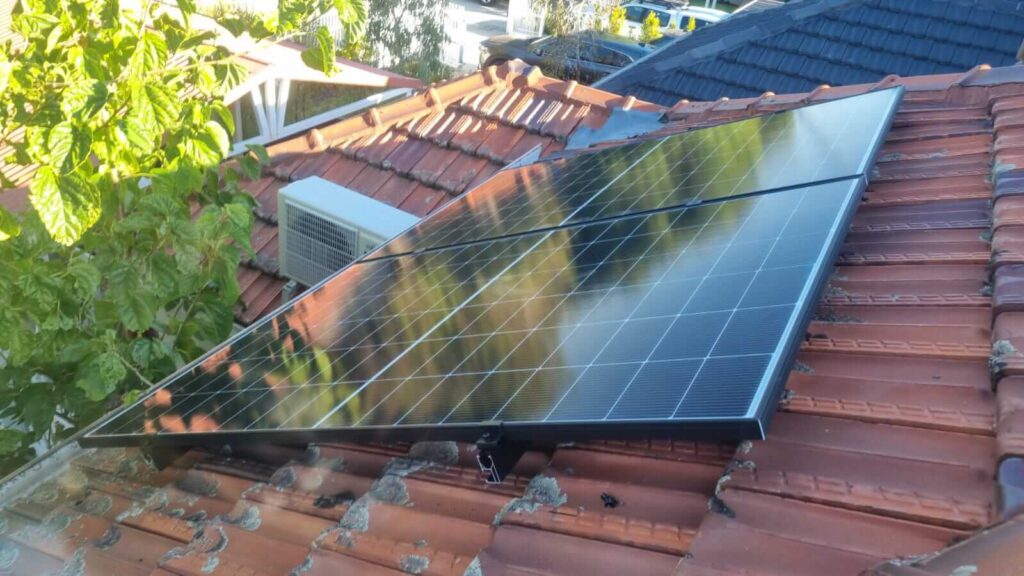 A 9.5kW solar panel is mounted on a red tiled Wembley roof, reflecting nearby trees and sky. Next to the panel, an air conditioning unit and a 40kWh battery storage system are also installed.