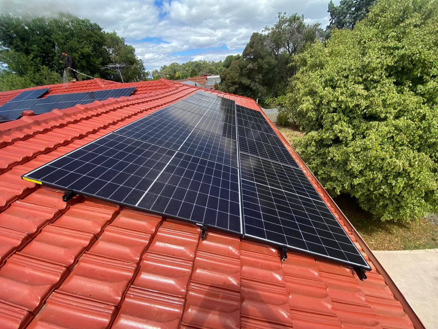 Solar panels on a red terracotta tiled roof among mature trees in Willetton