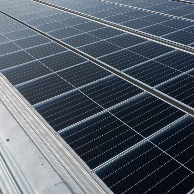 Rows of dark blue solar panels are installed on a metal rooftop, reflecting sunlight. The panels are aligned in parallel, efficiently capturing renewable energy—ideal for businesses seeking a Commercial Solar Quotation.